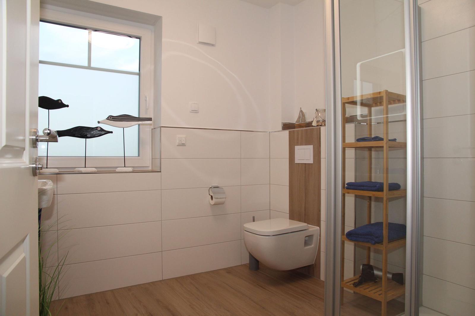 Badezimmer mit Toilette, Dusche und Fenster mit Vogeldekoration.