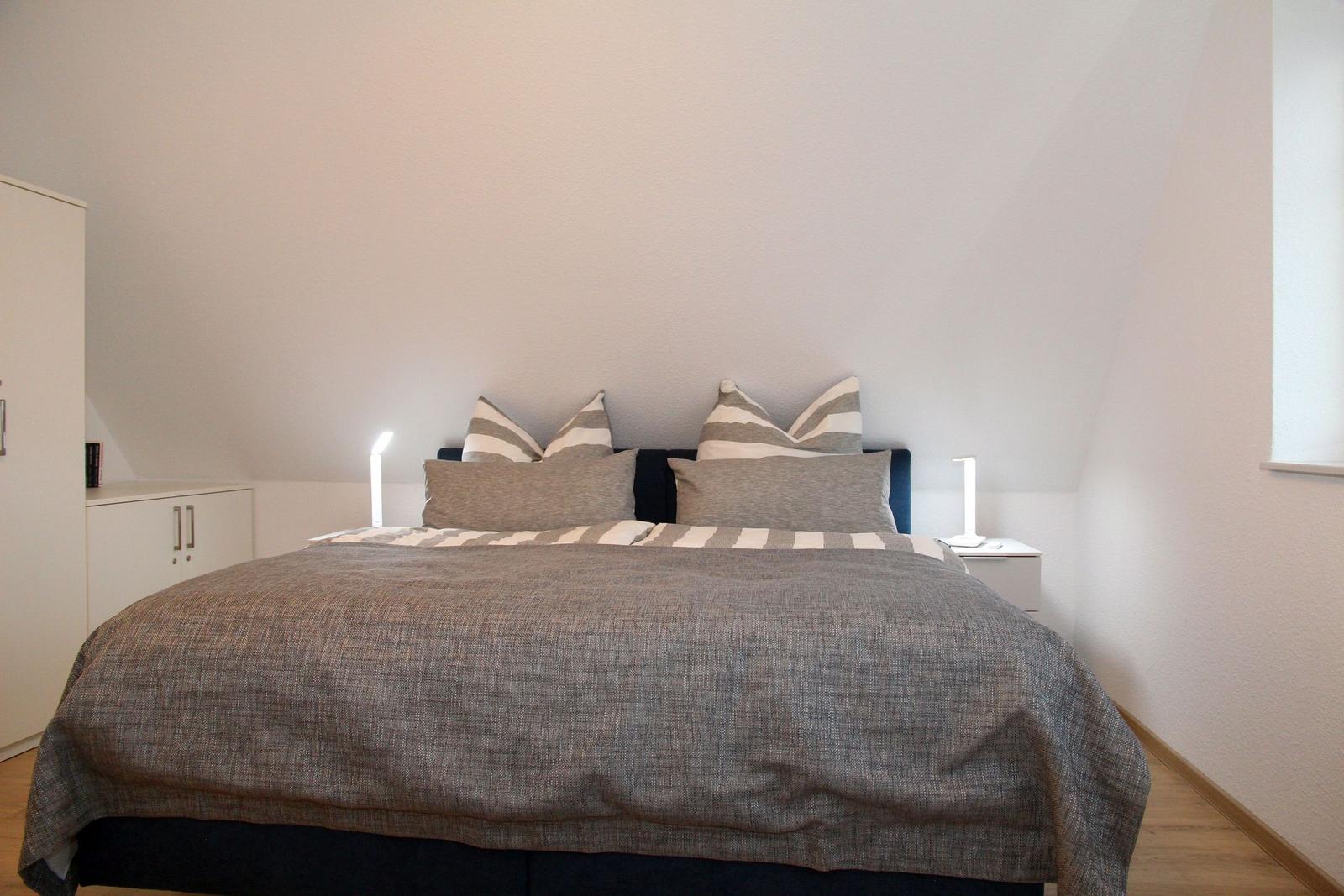 Schlafzimmer mit Bett, Nachttischen und Kleiderschrank. Wandfarbe weiß, Holzboden.