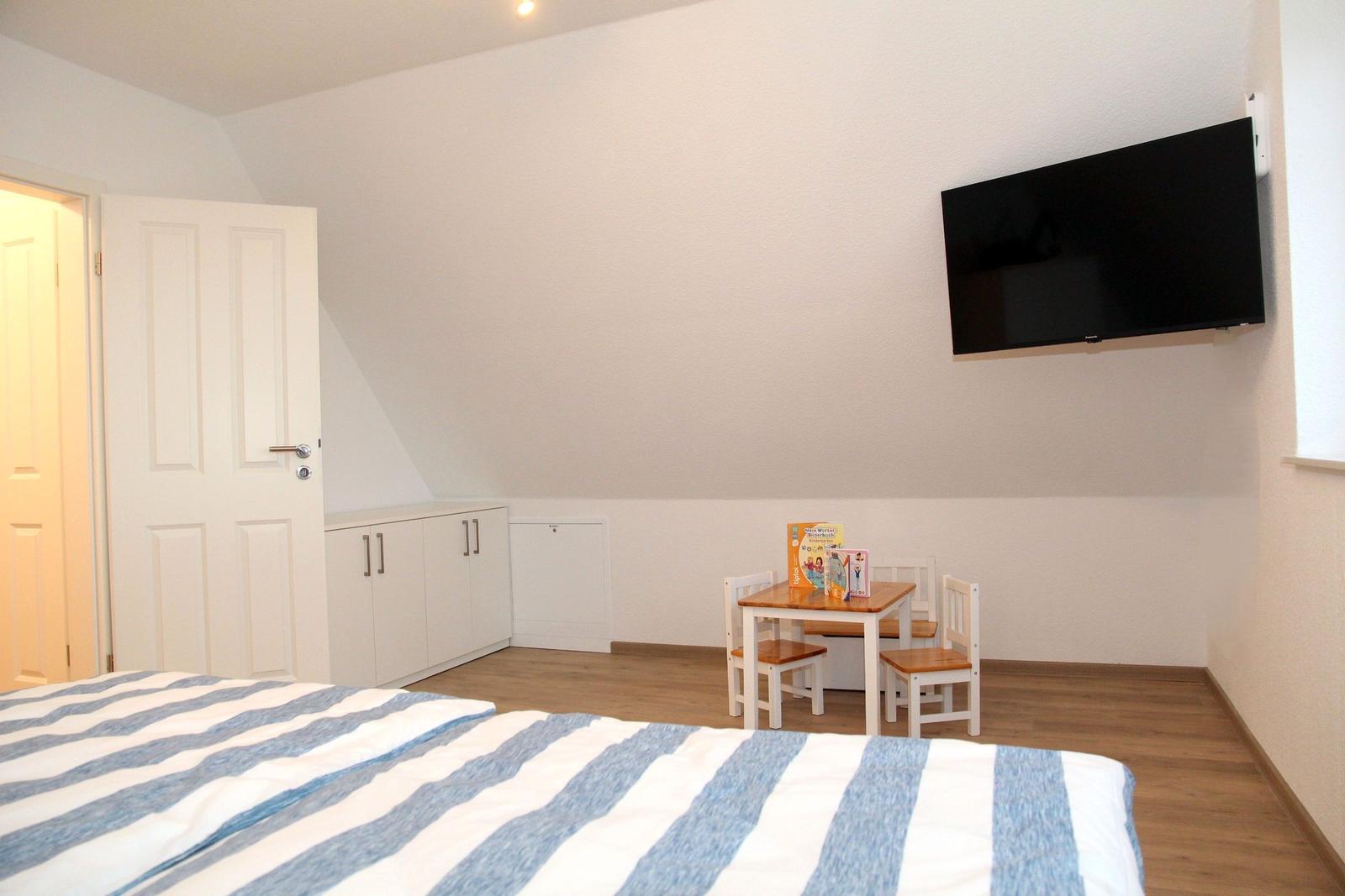 Schlafzimmer mit Bett, Kinderstuhl, TV und Schränken.