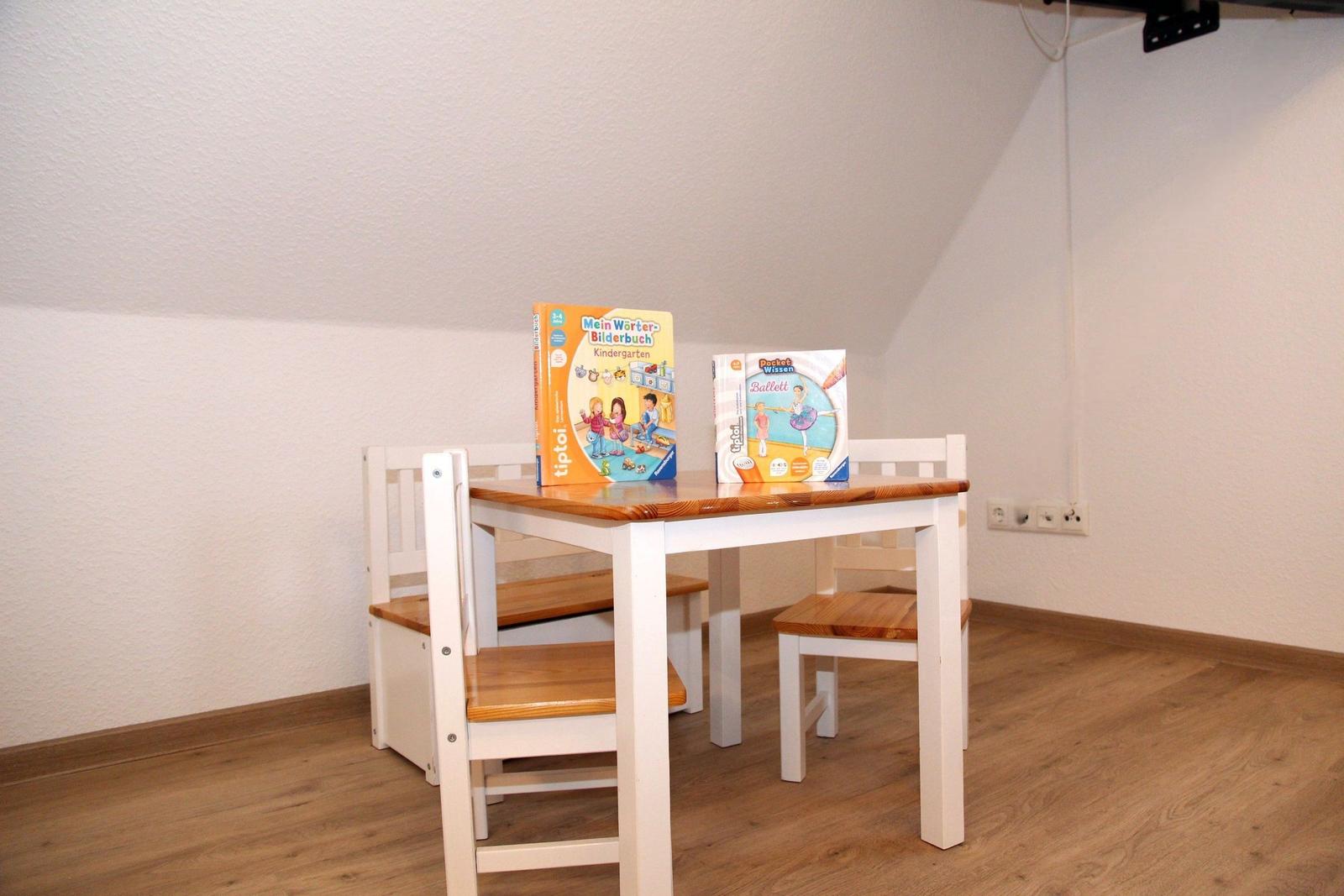 Kindertisch mit Stühlen und zwei Büchern auf Holzfußboden.