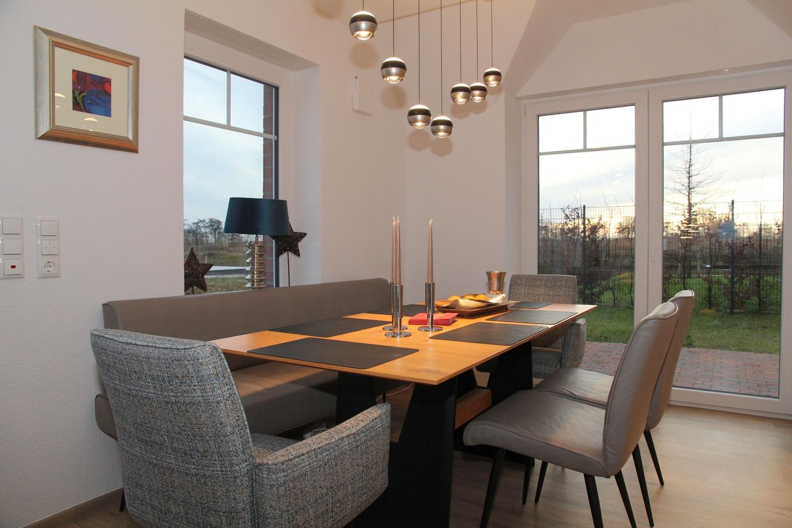 Esszimmer mit Tisch, Stühlen und Sitzbank. Fenster bieten Blick auf Garten.