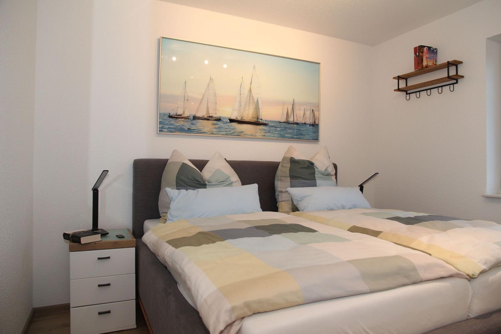 Schlafzimmer mit Bett, Nachttisch und Wandbild mit Segelbooten.