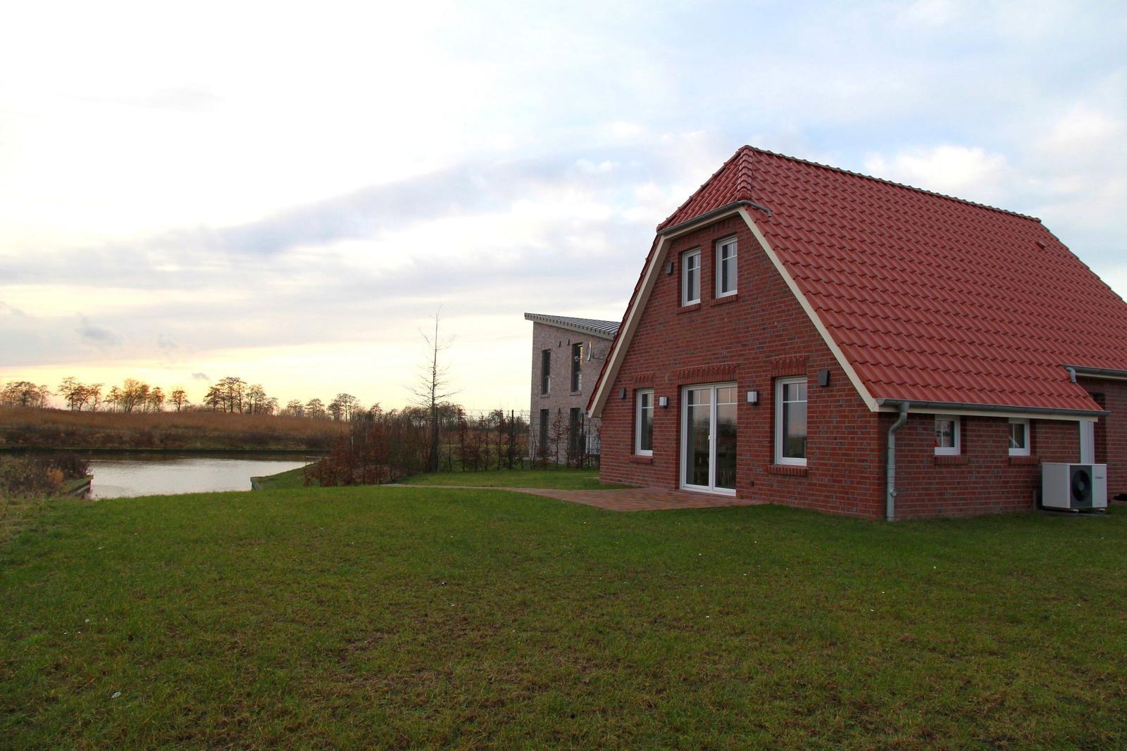 Rotes Ziegeldach, großer Garten und Wasser im Hintergrund. Modernes Haus mit Glasfront.