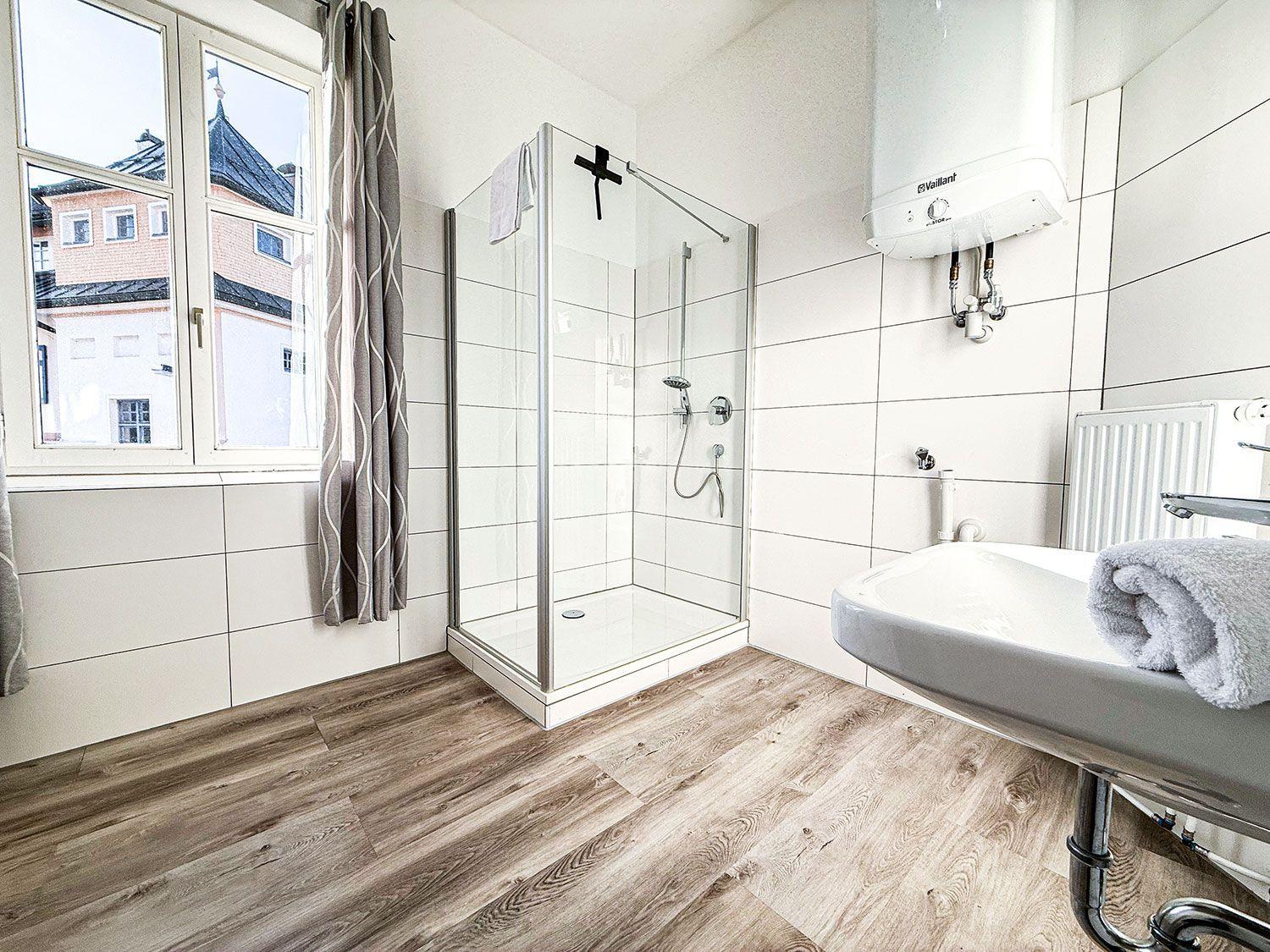 Badezimmer mit Dusche, Waschbecken und Fenster mit Blick auf Gebäude.