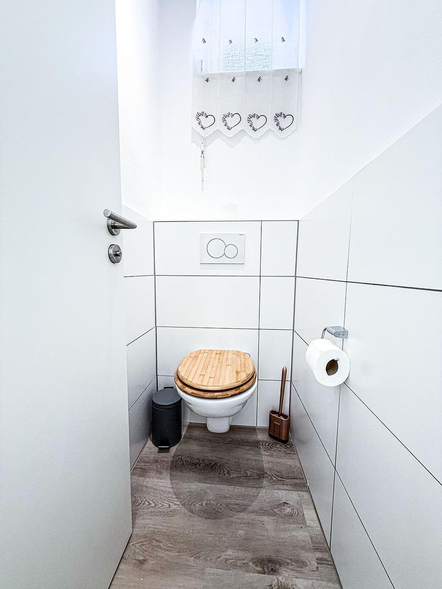 WC mit Holzdeckel, Toilettenpapierhalter und Fenster mit Herzvorhang