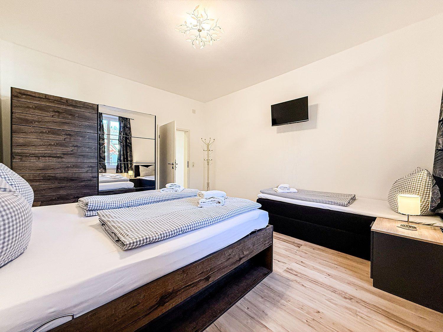 Zimmer mit Doppelbett, Schlafcouch, Fernseher und Spiegelschrank.