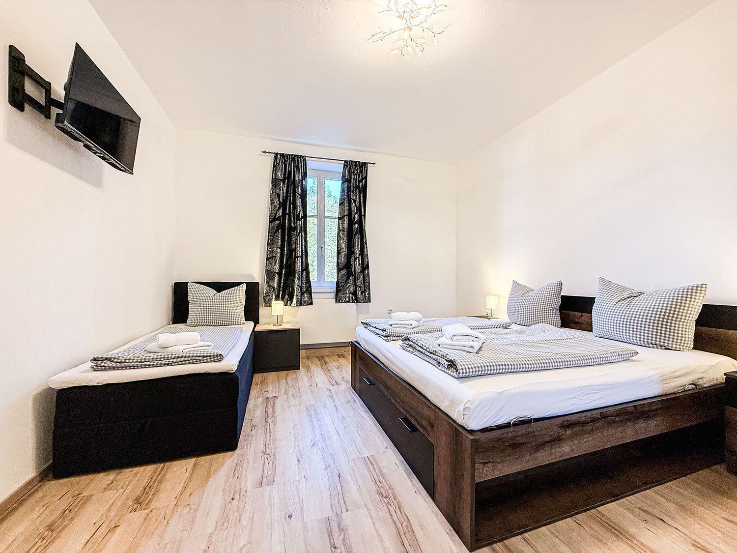 Zimmer mit zwei Betten, Fenster, TV und Holzboden.