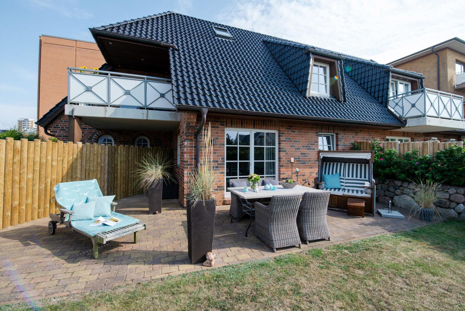 Terrasse mit Sitzgruppe, Liege und Balkon an einem Haus mit Ziegelfassade.