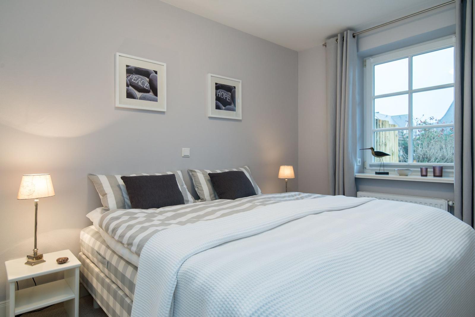 Schlafzimmer mit Bett, zwei Nachttischen und Fenster mit Vorhängen.