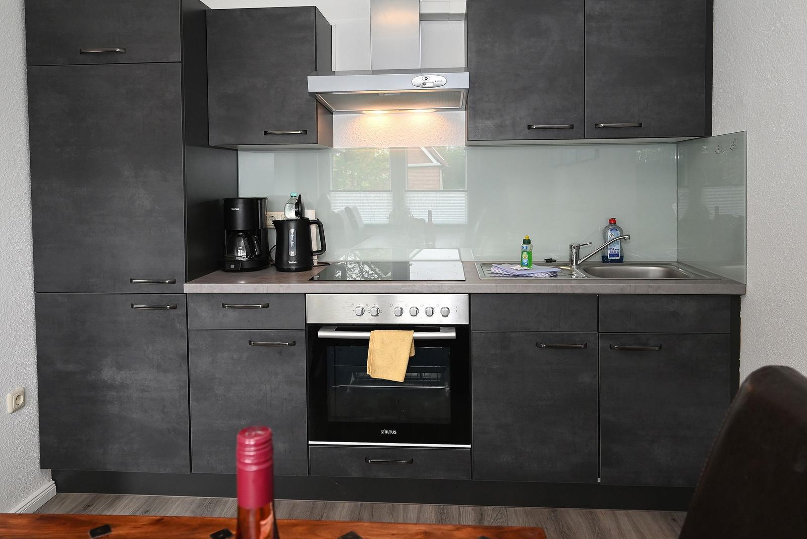 Küche mit dunklen Schränken, Herd, Spüle und Dunstabzug.