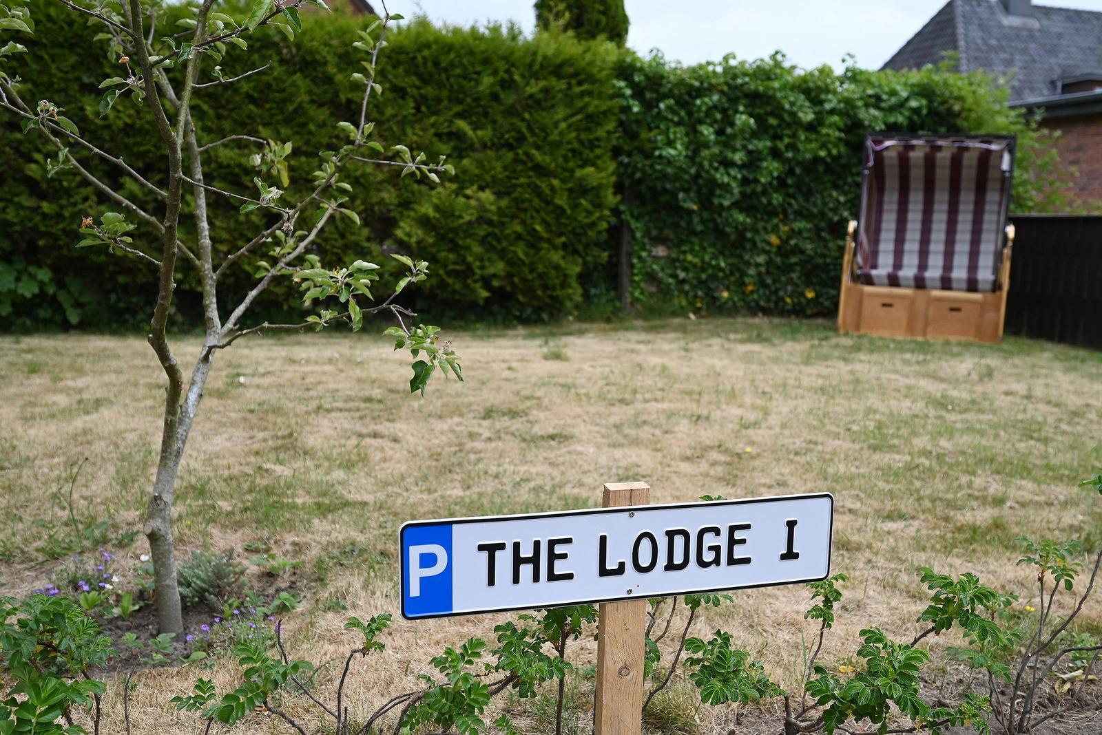 Schild mit Parkplatz für The Lodge 1, Rasenfläche mit Stuhl und Hecke im Hintergrund.