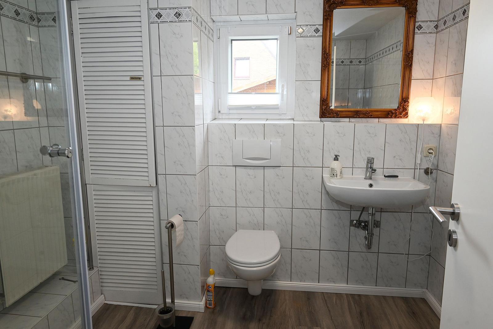 Badezimmer mit Dusche, Toilette und Waschbecken. Fliesenwand und Holzboden.