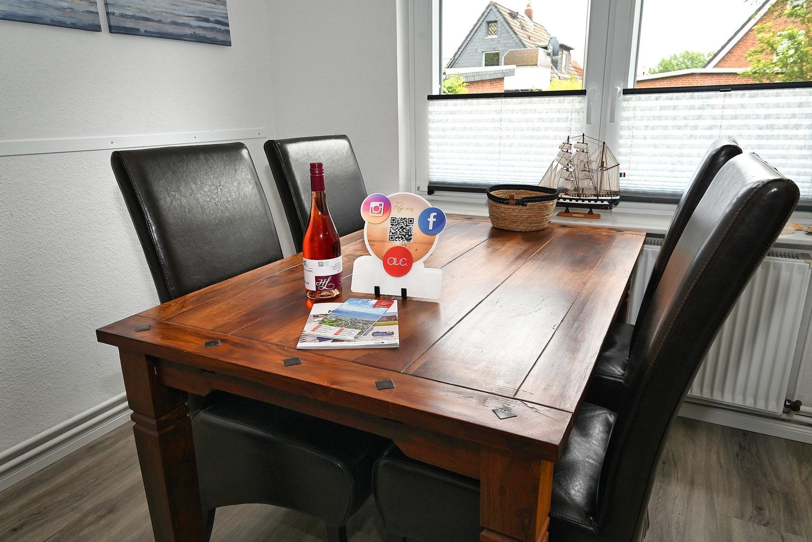 Holztisch mit vier Stühlen, Flasche, Prospekt und Modellboot am Fenster