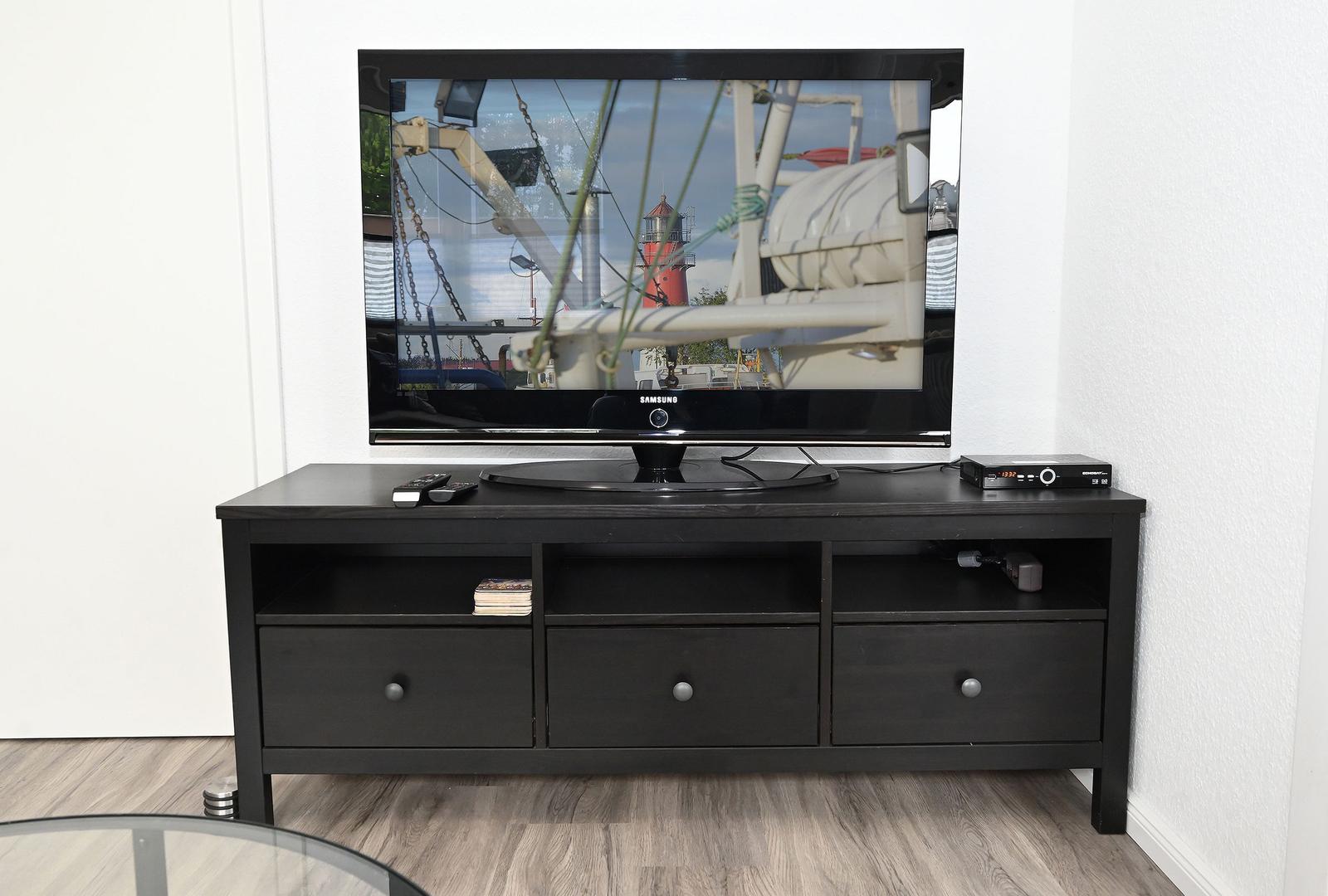 Flachbildfernseher auf schwarzer TV-Einheit mit Fernbedienungen und Receiver.