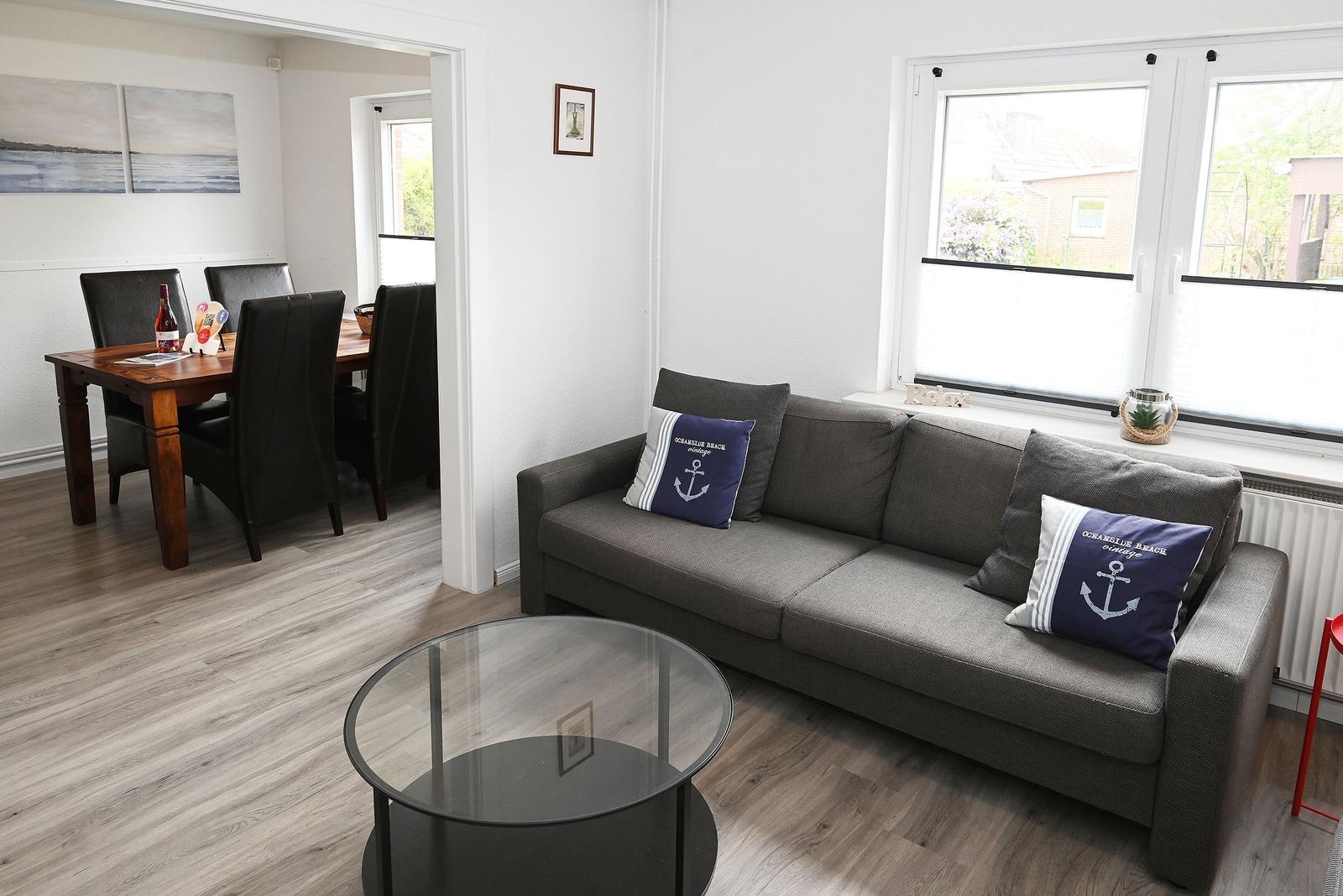 Wohnzimmer mit grauem Sofa, Glas-Tisch und Blick auf Terrasse.