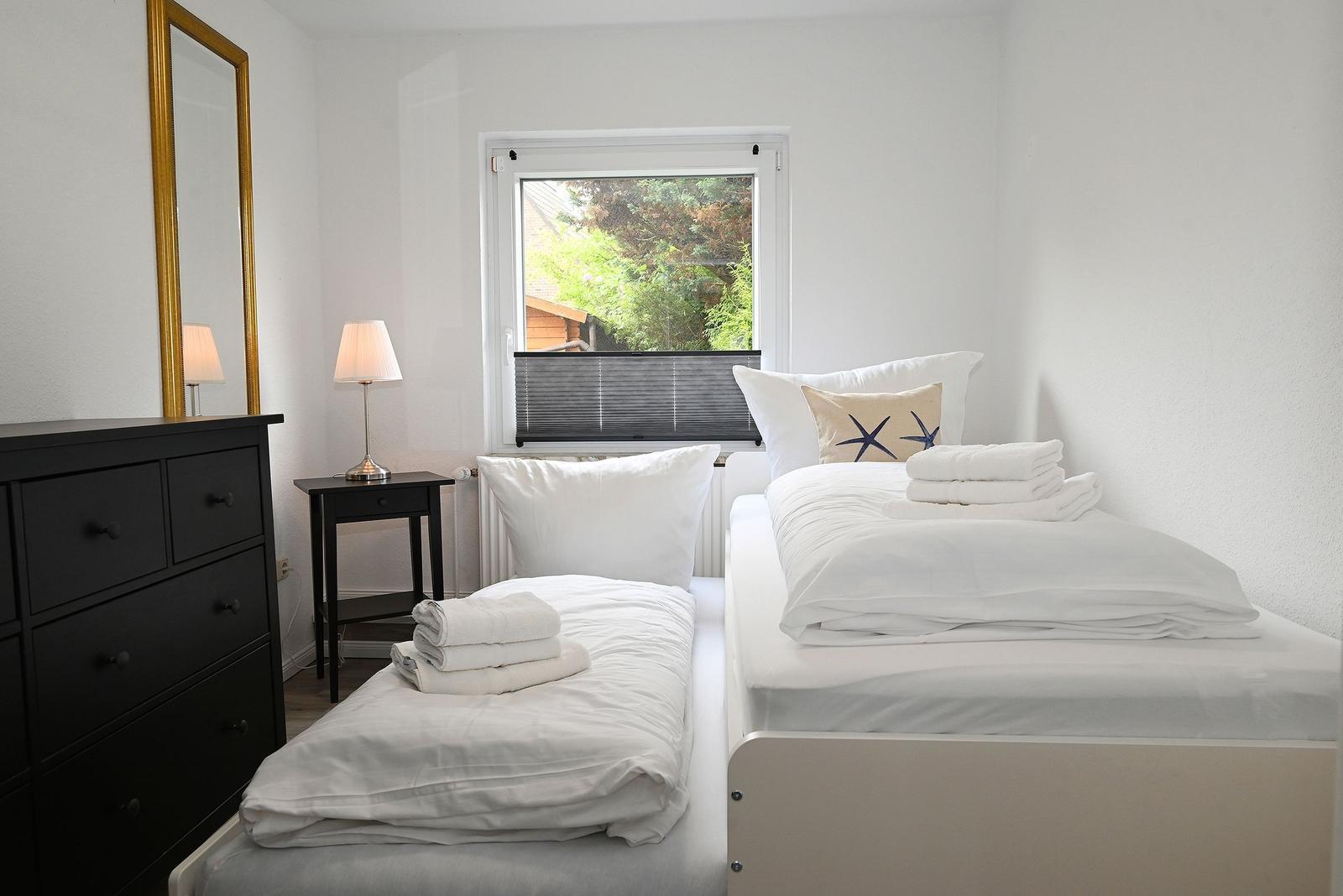 Zimmer mit zwei Betten, Schrank, Nachttisch und Fenster mit Blick auf Grün.