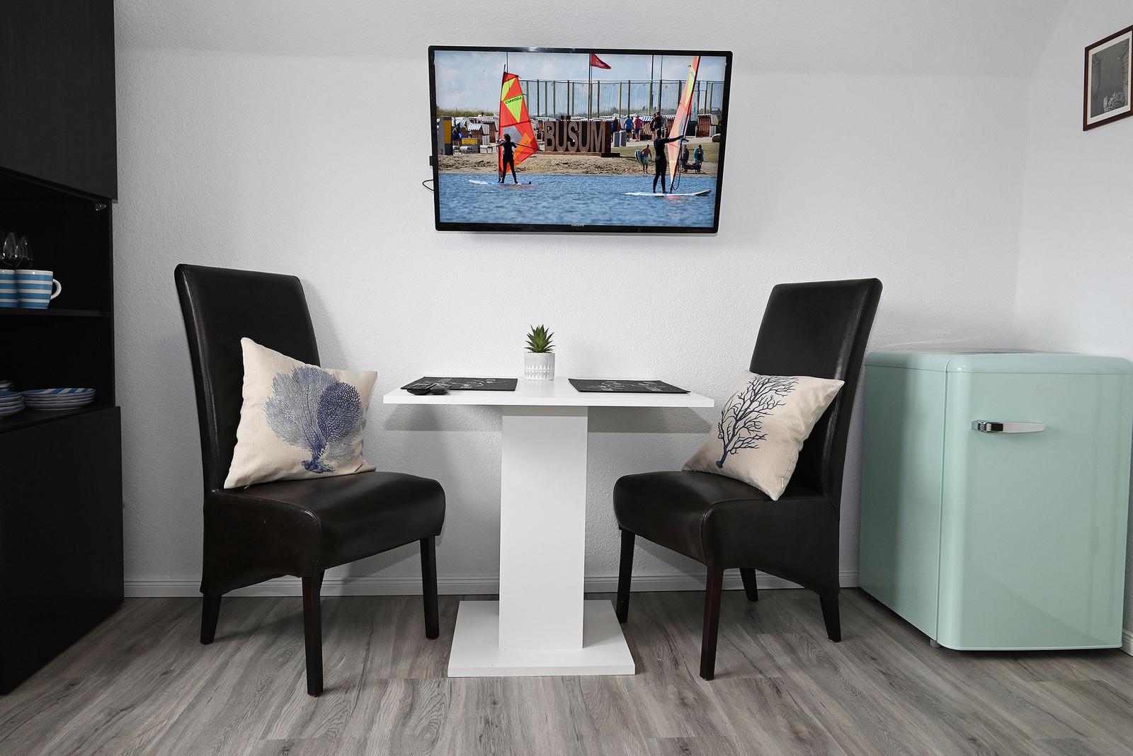 Esstisch mit zwei Stühlen, Fernseher und Kühlschrank in einem Raum.