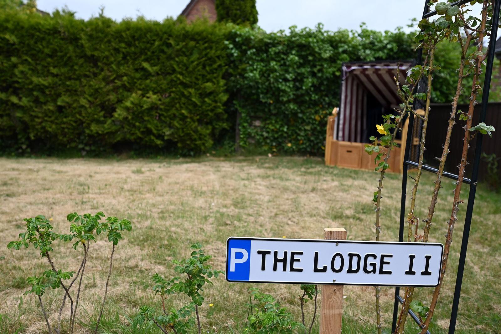 Schild mit Parkplatz für The Lodge 11. Hintergrund: Rasen, Hecke und Pavillon.
