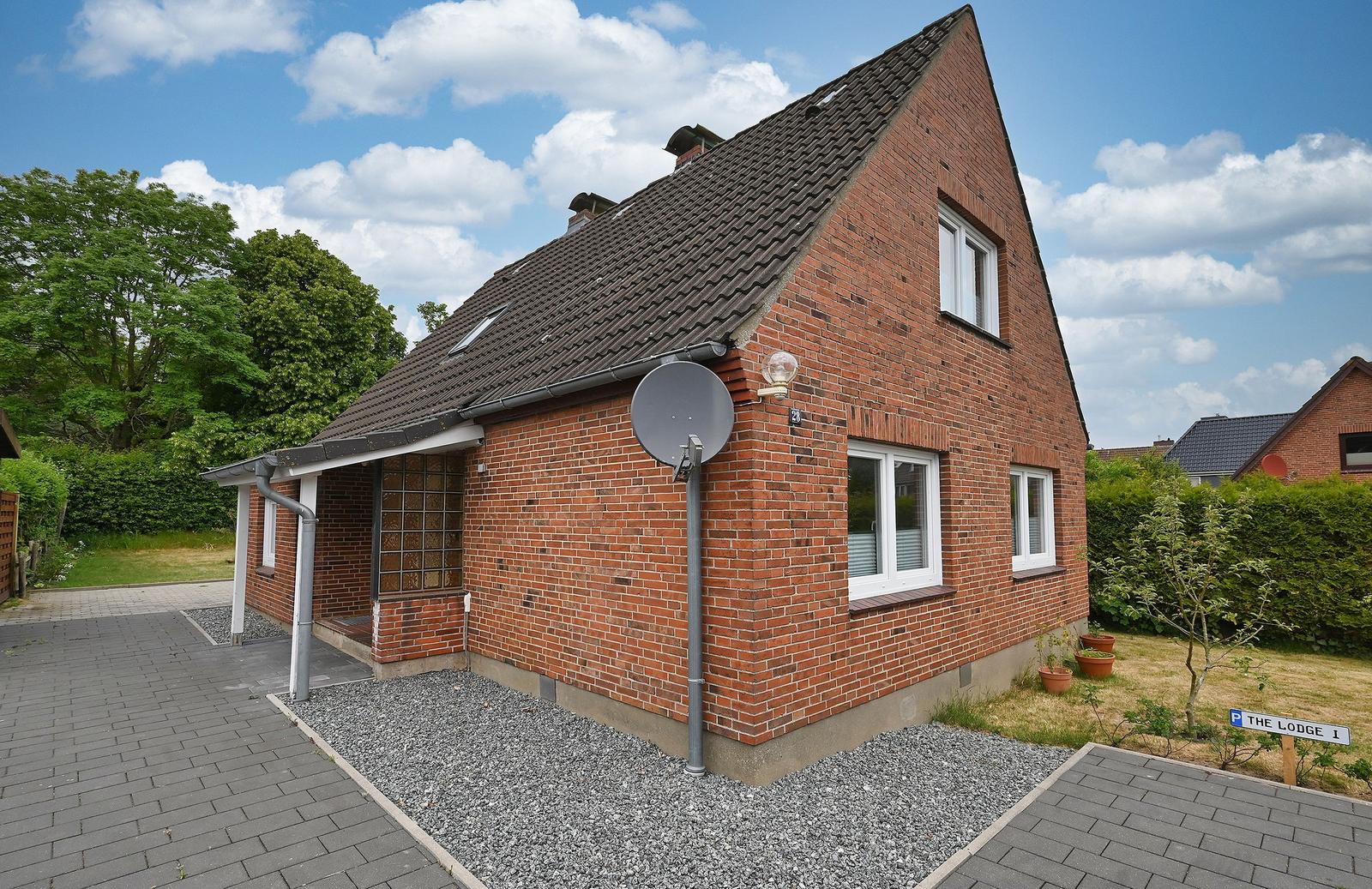 Rotes Backsteinhaus mit Dach, Fenstern und Satellitenantenne. Vorgarten mit Steingarten und Schild.
