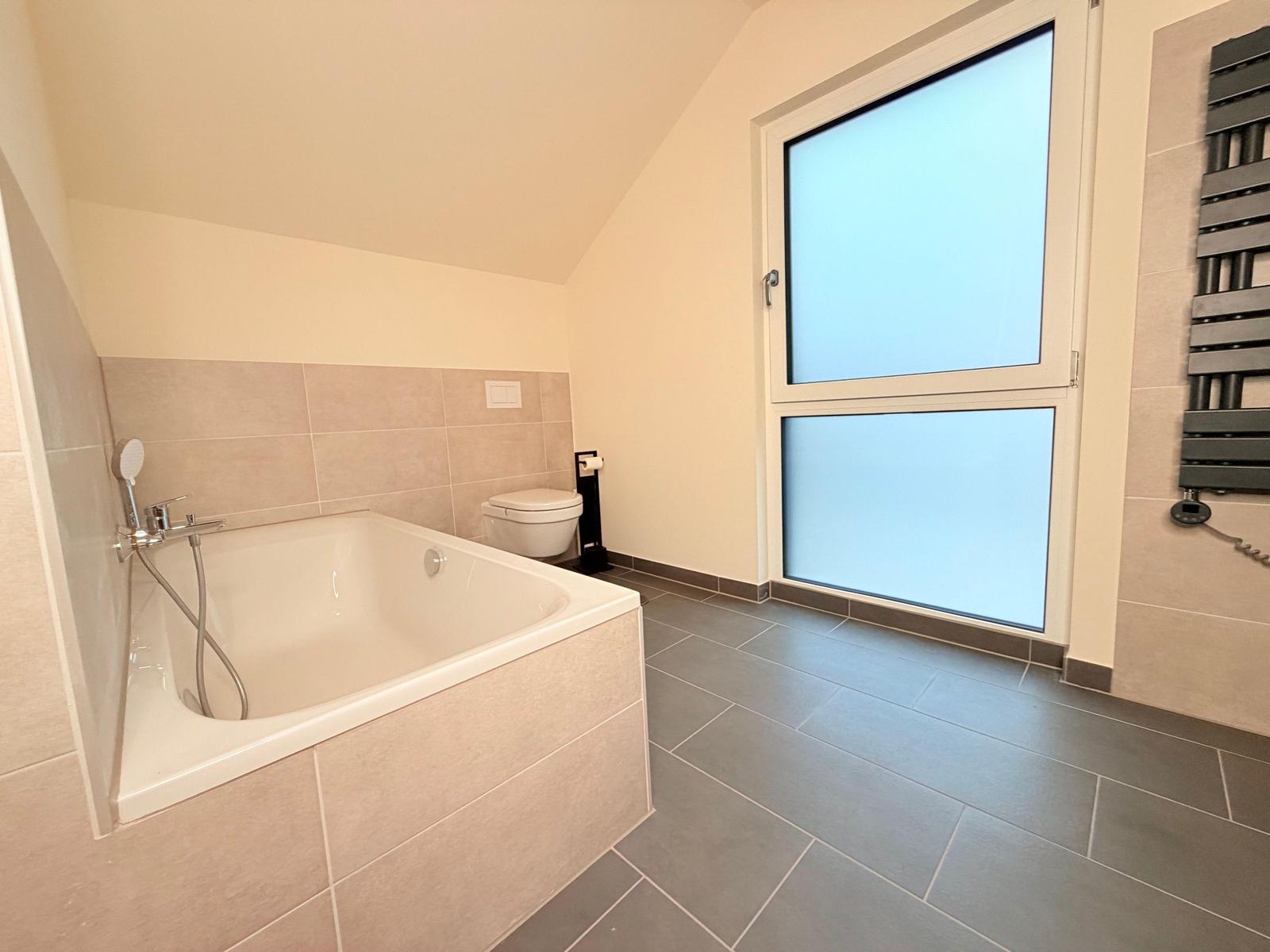 Badezimmer mit Badewanne, Toilette und großen Fenstern.