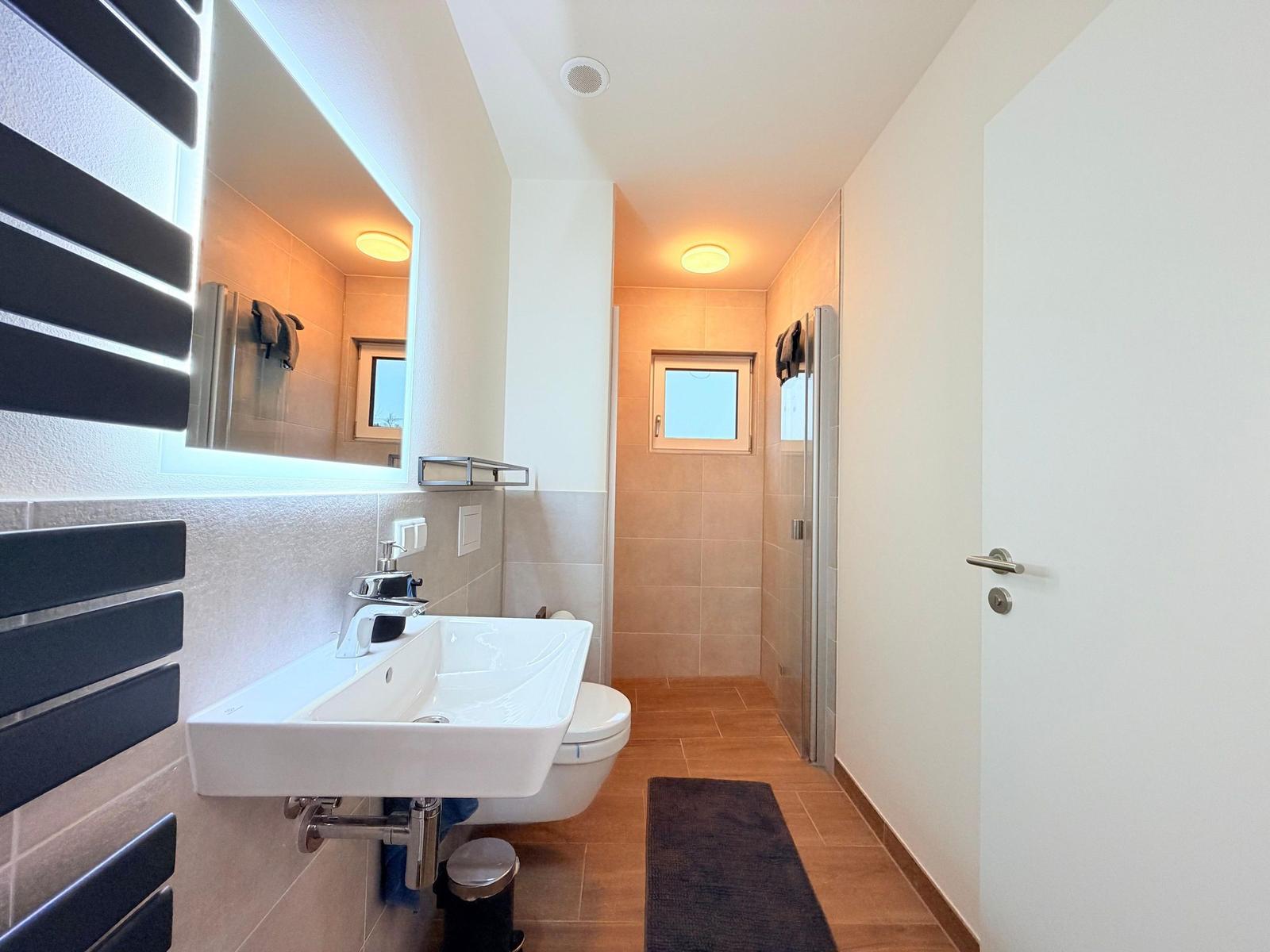 Badezimmer mit Waschbecken, Toilette, Dusche und Heizkörper.