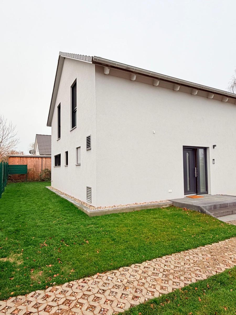 Moderne Villa mit Garten und Terrasse. Schwarze Fenster und Tür. Grasfläche und Kiesweg.