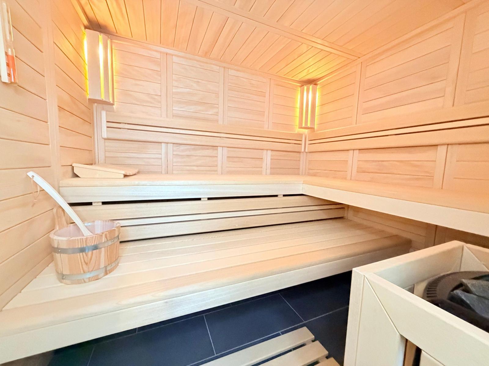Sauna mit Holzbank, Eiche, Eimer und Deckenbeleuchtung.