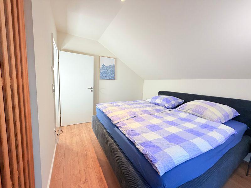 Schlafzimmer mit Doppelbett, Holzboden und schräger Decke. Tür und Wandbild sind sichtbar.