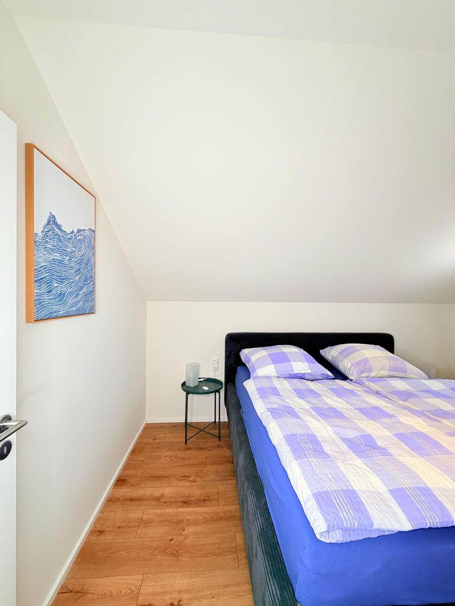 Schlafzimmer mit Doppelbett, Holzboden und Wandbild. Nachttisch neben dem Bett.