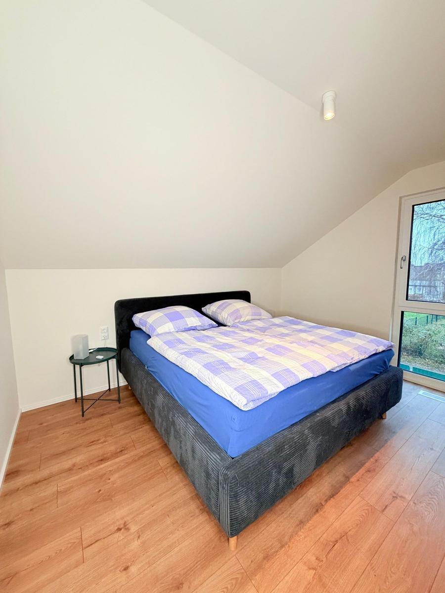 Schlafzimmer mit Doppelbett, Holzboden und Dachfenster. Bett mit blauer Matratze und kariertem Bettbezug.
