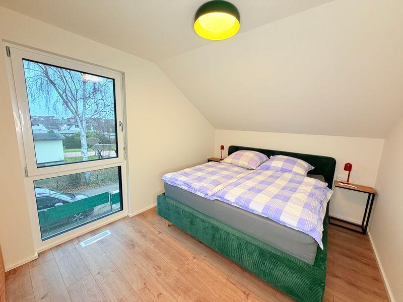 Schlafzimmer mit Doppelbett, grüner Bettumrandung und Fenster mit Blick nach draußen.