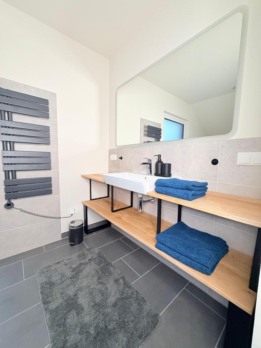 Badezimmer mit Waschbecken, Spiegel, Handtuchhalter und Heizkörper an der Wand.