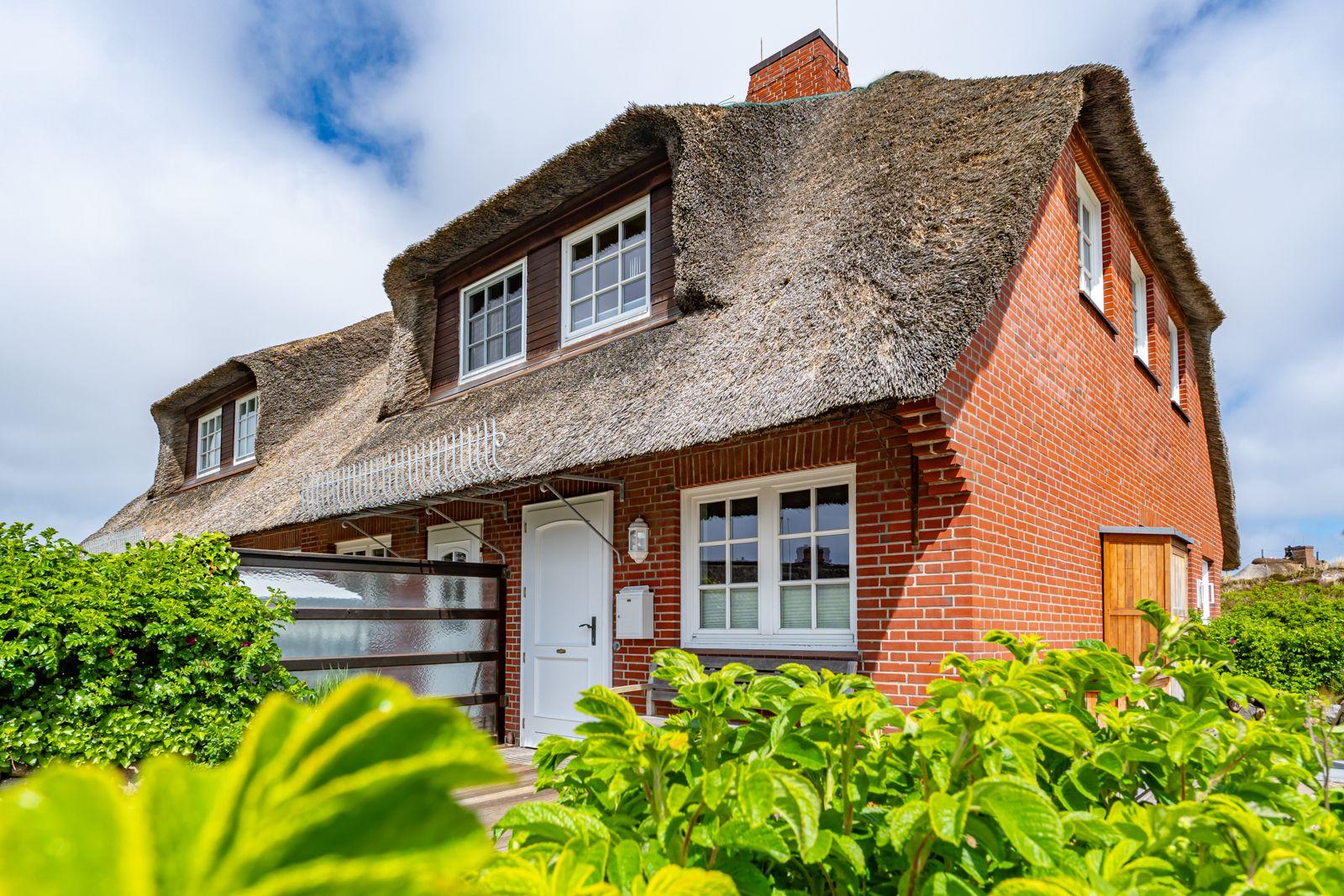 Rotes Backsteingebäude mit Strohdach und weißen Fenstern. Grünflächen im Vordergrund.