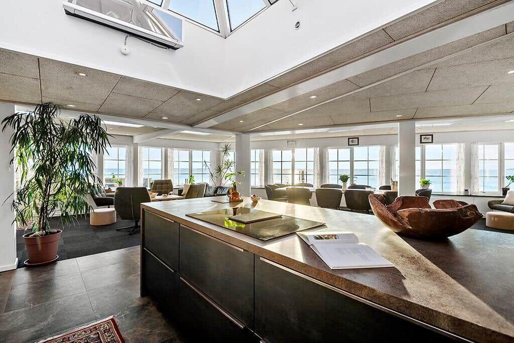 Kitchen with sea view, large windows, plants, and wooden bowl.