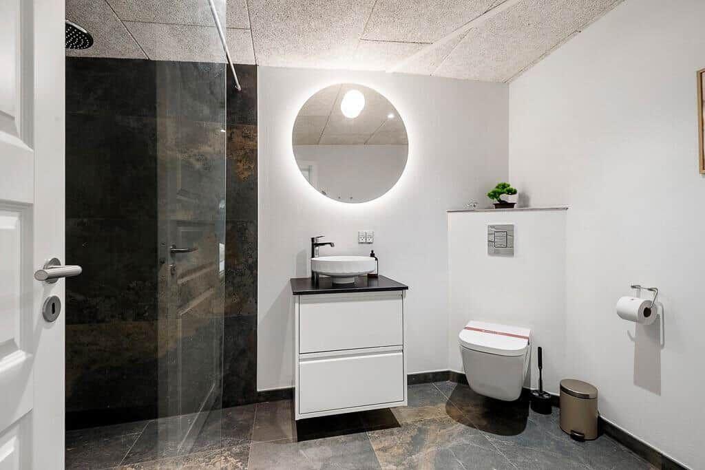 Bathroom with shower, sink and toilet. Round mirror with lighting.