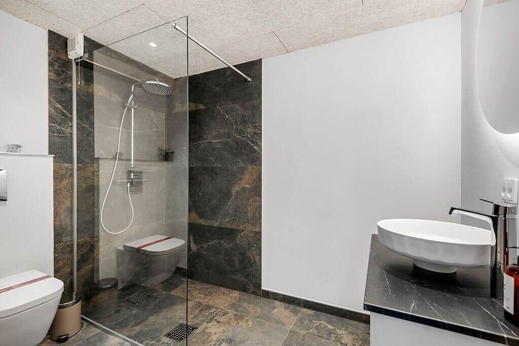 Bathroom with shower, sink and toilet. Marble walls and floor tiles.