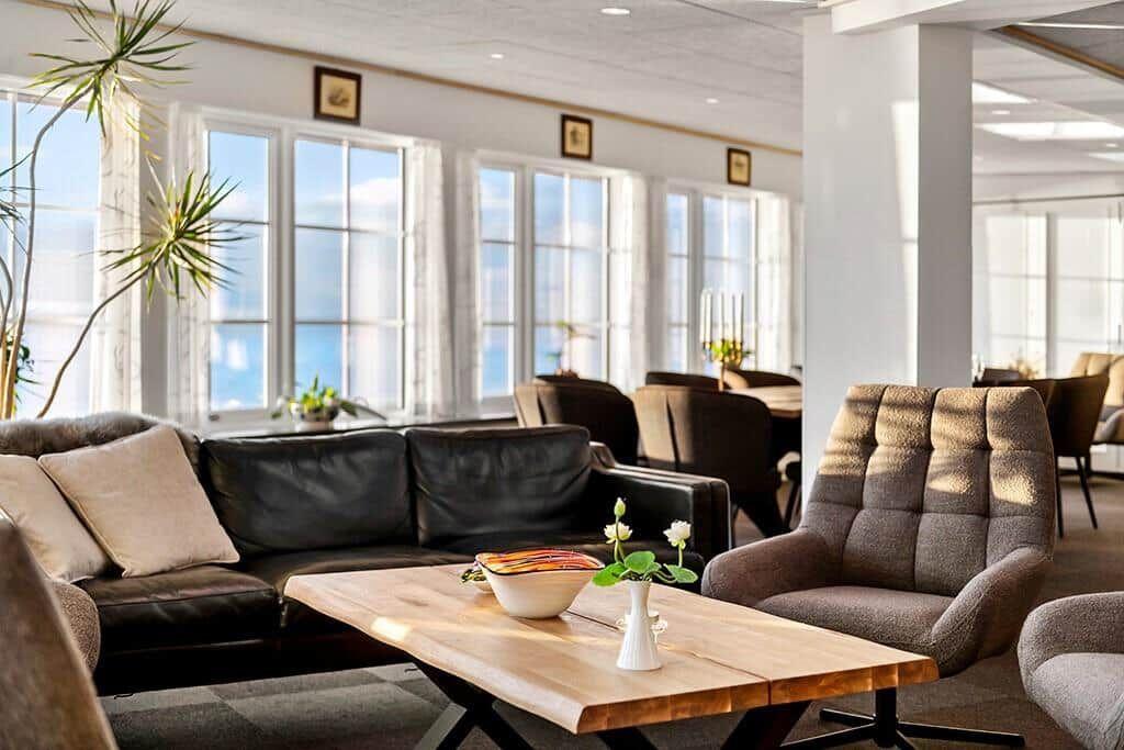 Living area with sofa, chairs, and table. Large windows with water view.
