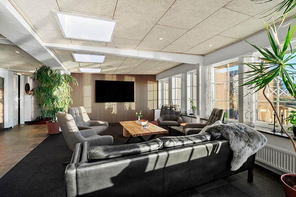 Living room with sofa, armchairs, wooden table, and large windows.
