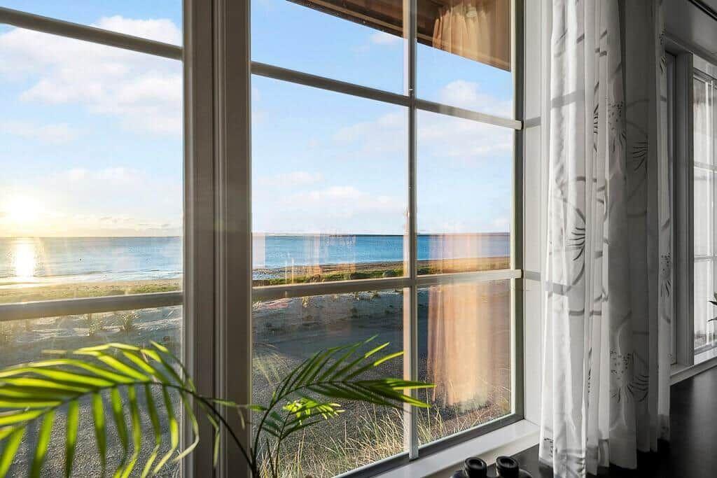 Large window with view of beach and sea at sunset.