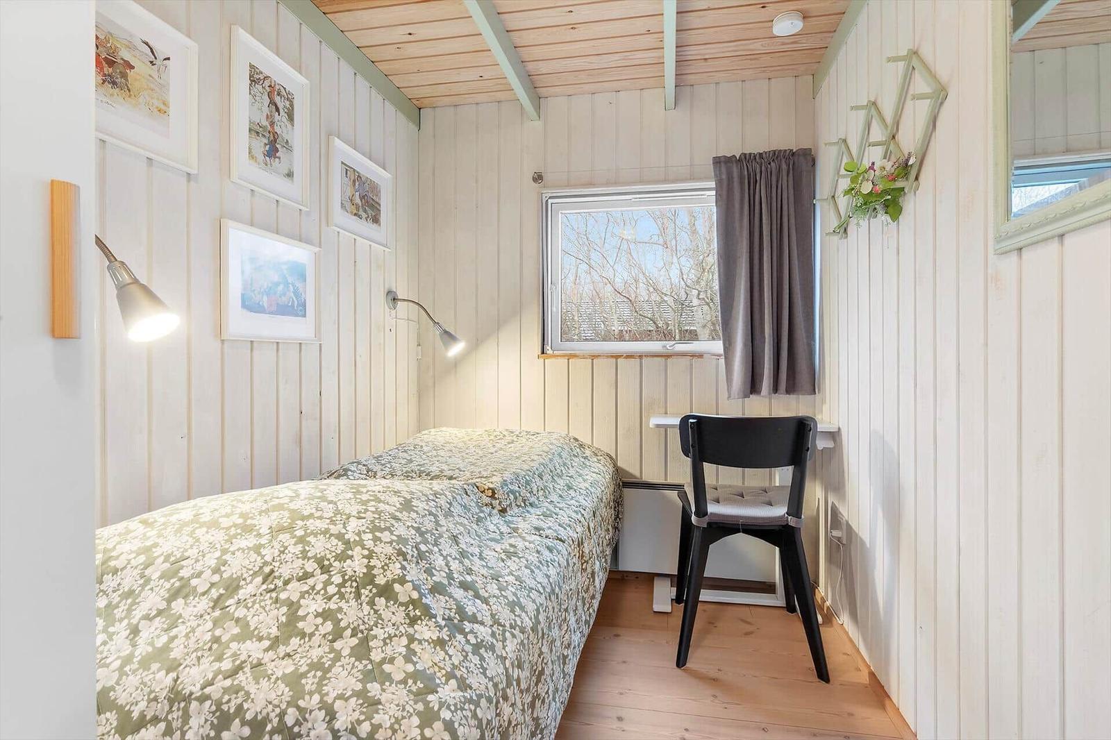 Bedroom with bed, desk, and window. Walls made of wood, pictures on the wall.
