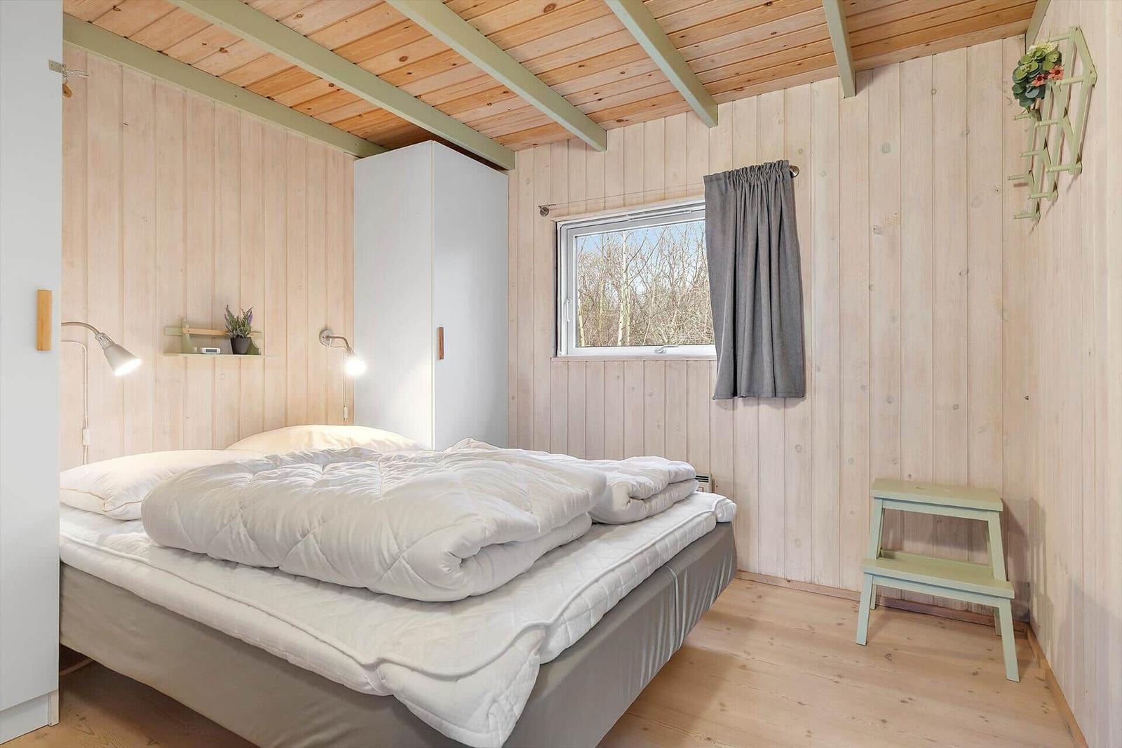 Bedroom with wooden walls, bed, wardrobe, and window with curtain.