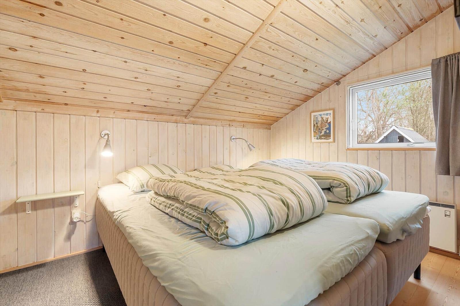 A bedroom with wooden walls, a bed, and a window.