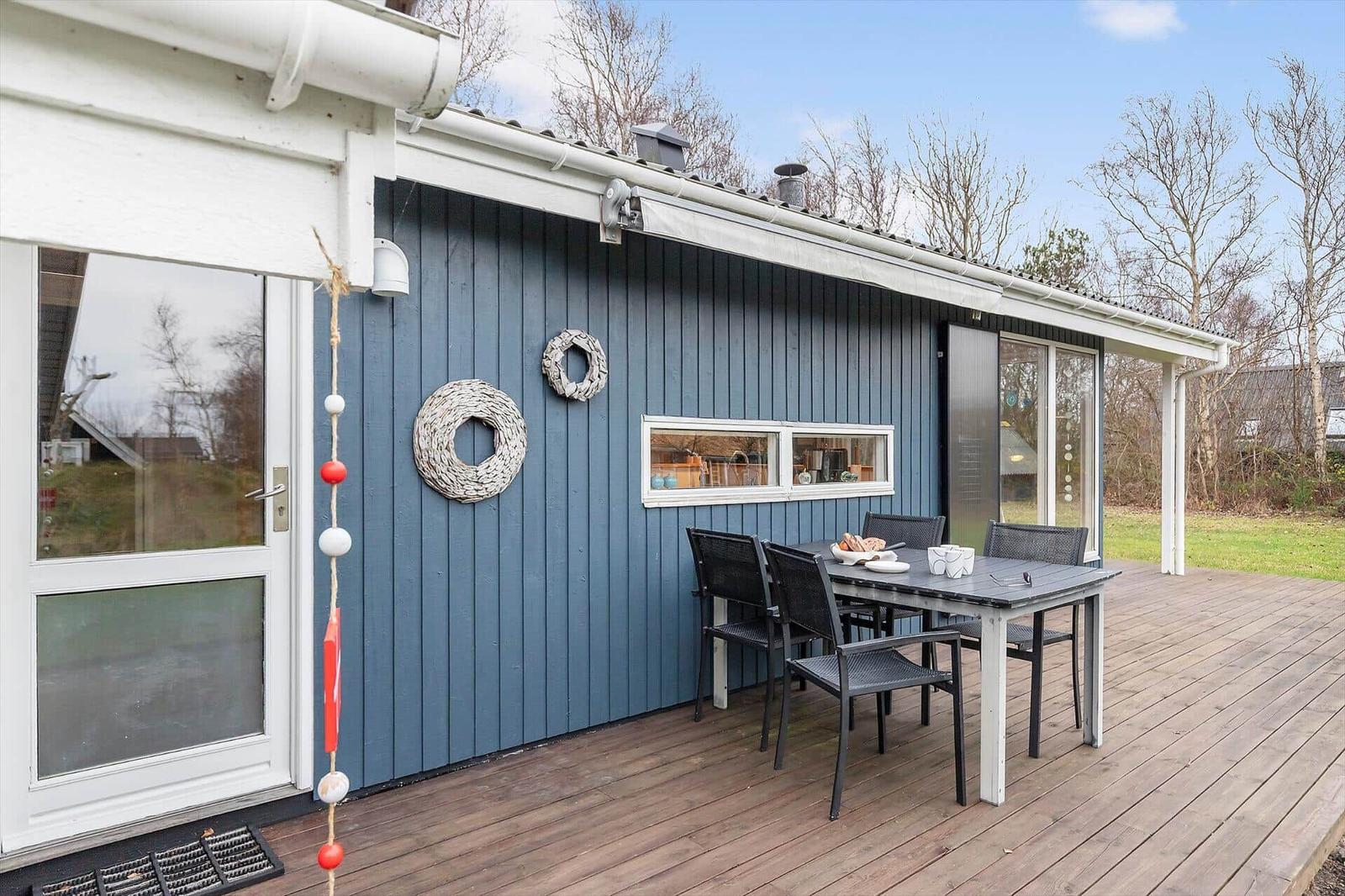 Deck with table and chairs in front of blue house with windows and decor.