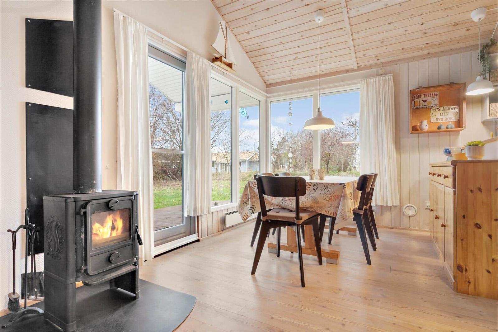 Room with stove, dining table, and large windows. Wooden ceiling and floor.
