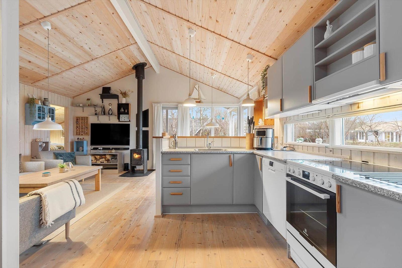 Kitchen with gray cabinets and wood ceiling. Living area with fireplace and TV.