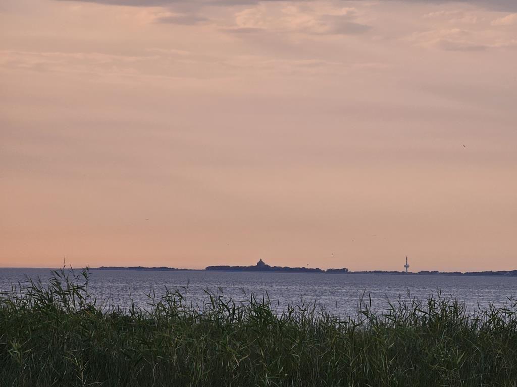Sonnenuntergang über dem Wasser mit Insel und Fernsehturm im Hintergrund.
