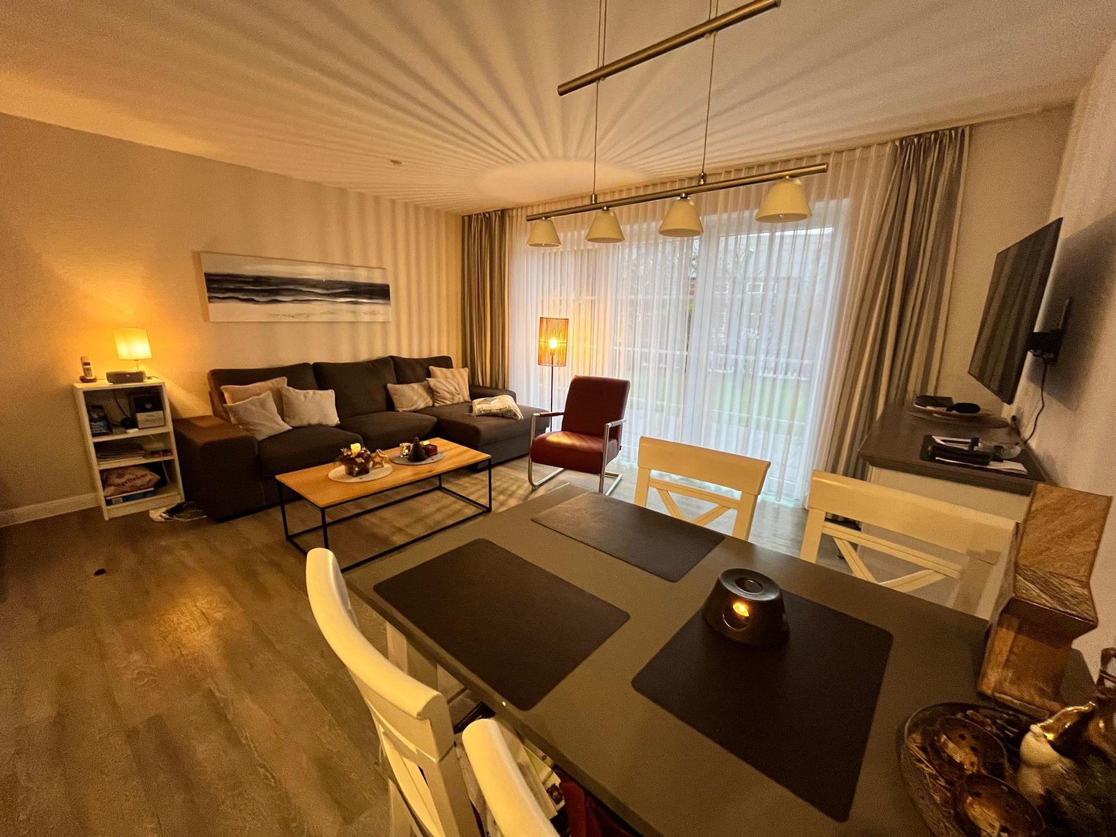 Ein modernes Wohnzimmer mit einem gemütlichen Sofa, einem Sessel und einem Couchtisch. Ein Essbereich mit einem Tisch und  4 Stühlen