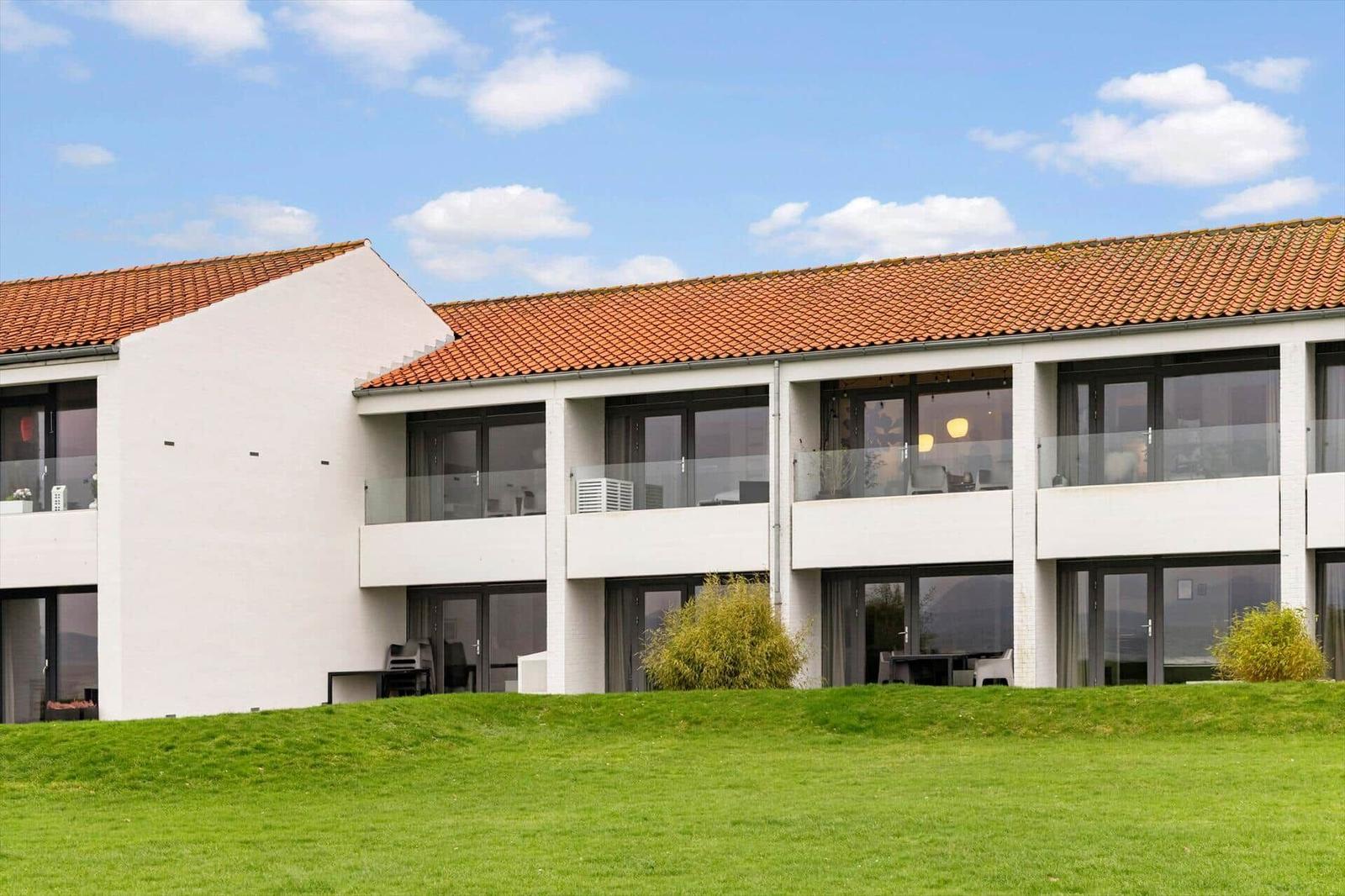 Modern holiday home with balconies and red tiled roof on green lawn.