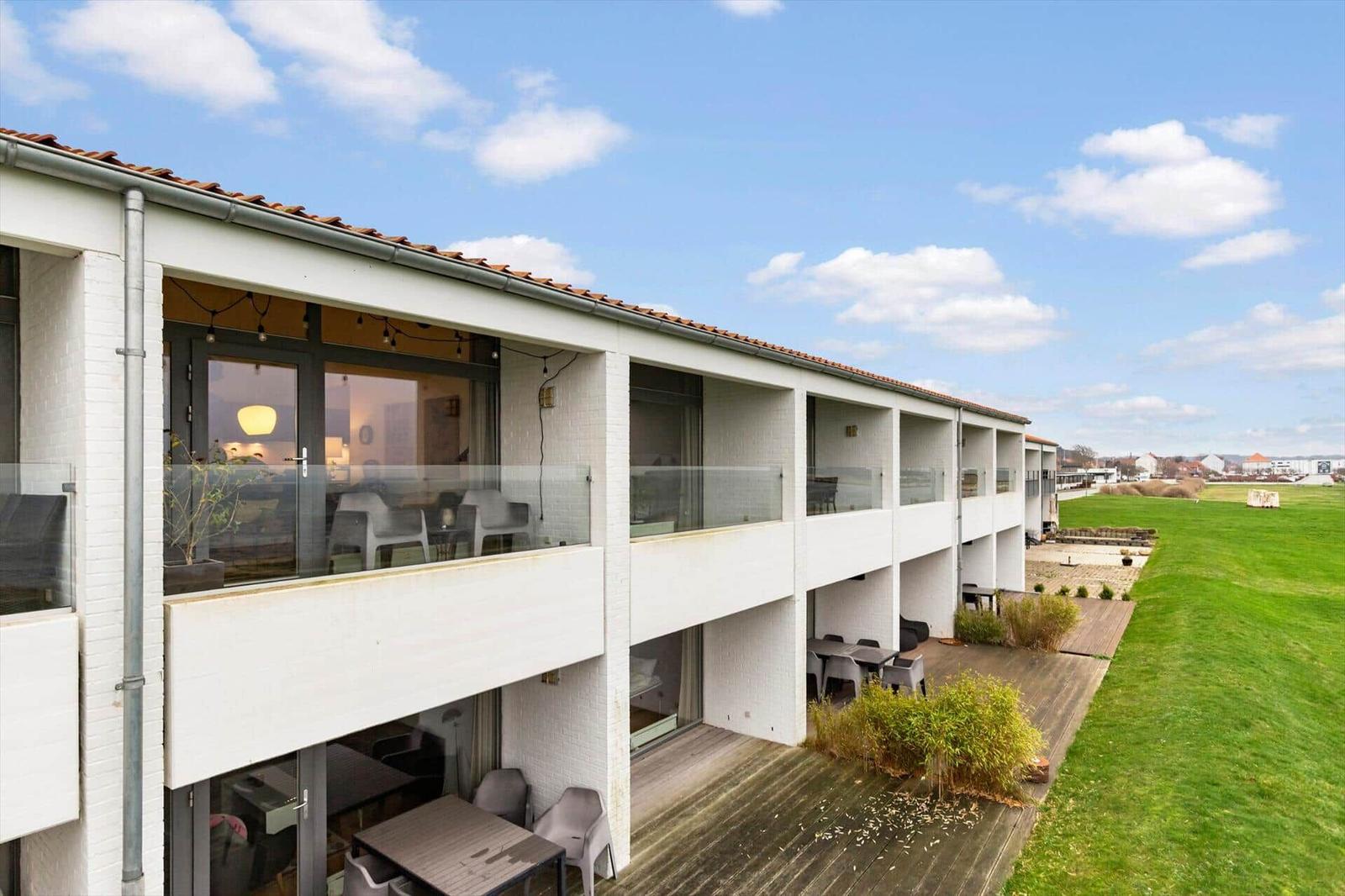 Modern vacation apartment with balcony and terrace. View of green field under blue sky.