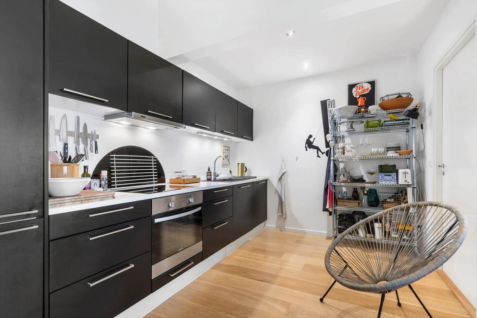 Kitchen with black cabinets, wooden floor, and metal shelf. A round seating area is in the room.